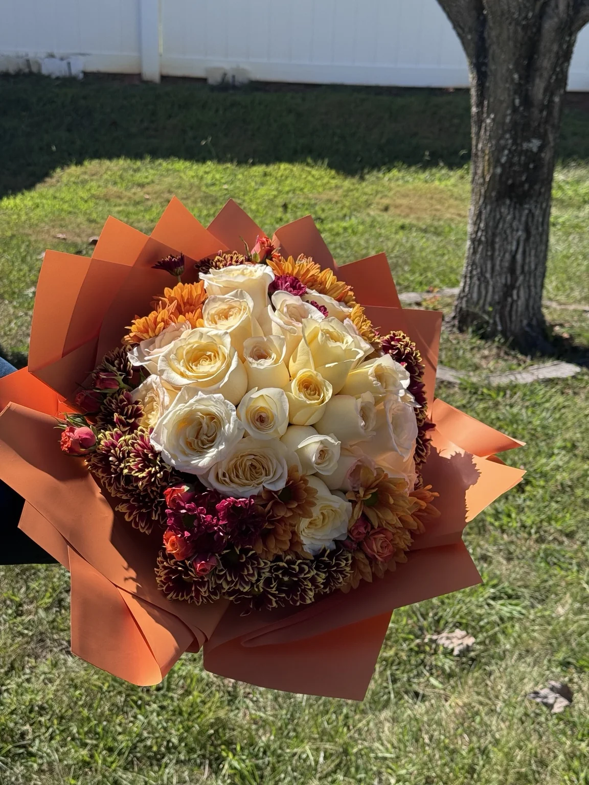Cream roses with warm orange wrap and a bright sunflower accent